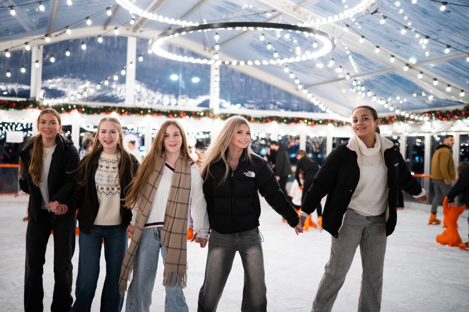 Friends skating hand in hand under fairy lights on the covered ice rink