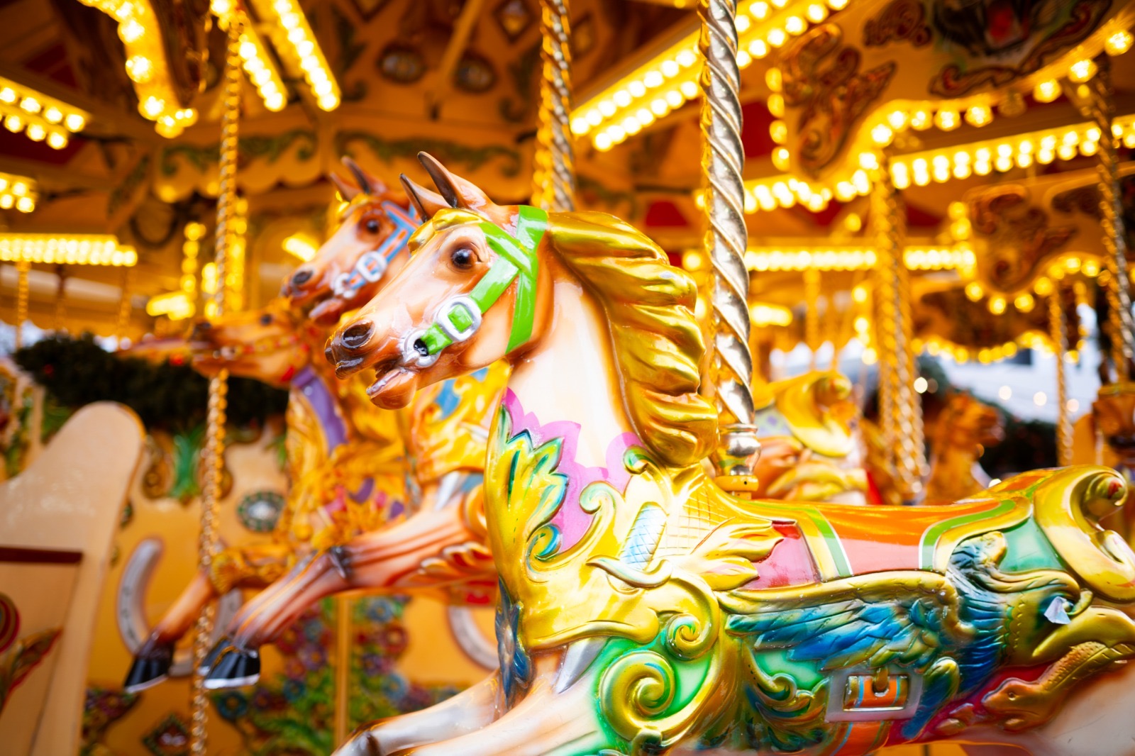 Brightly painted horses on the vintage carousel lit with golden bulbs