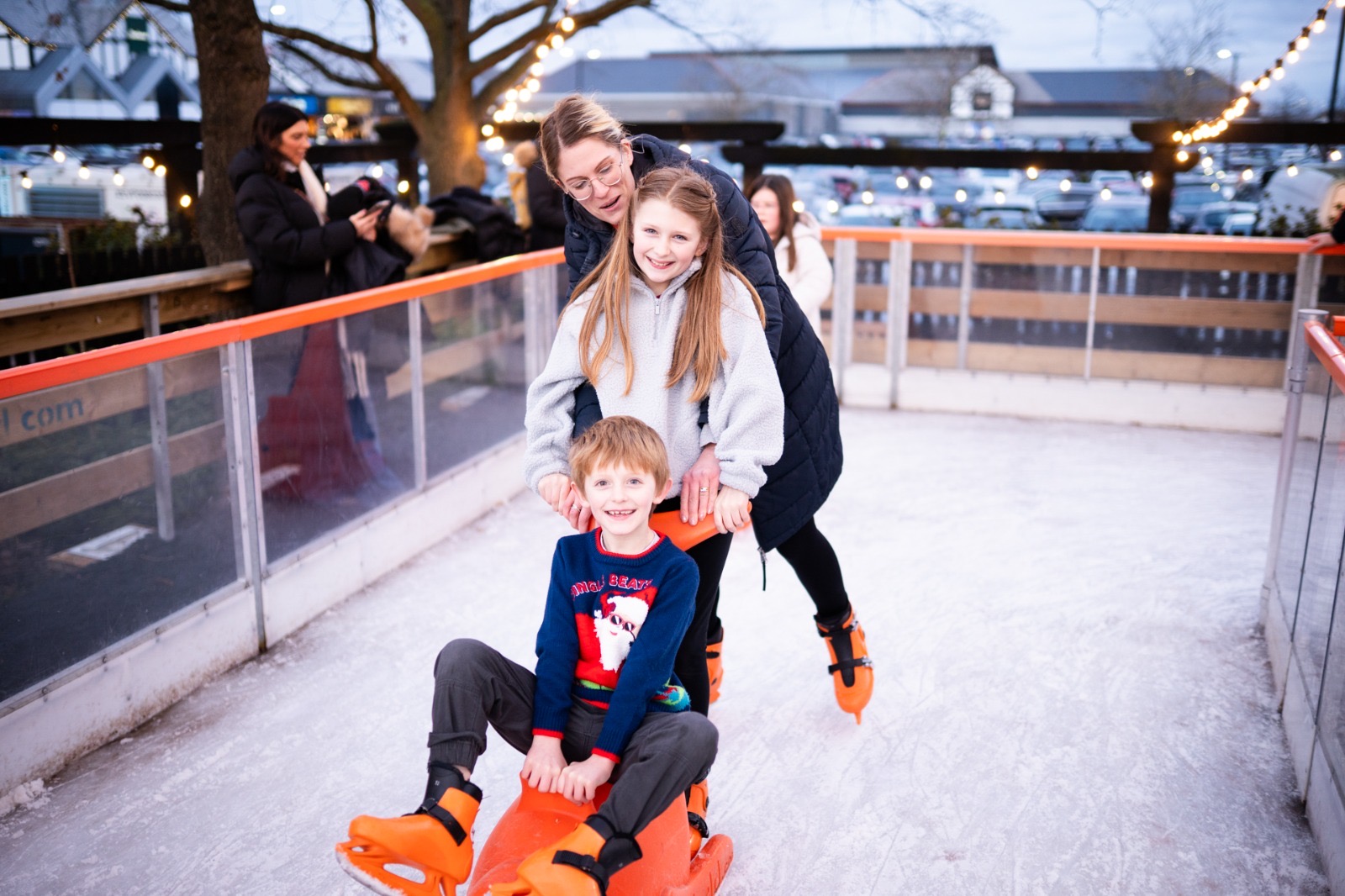 A family skating together with a skate aid at the outdoor rink