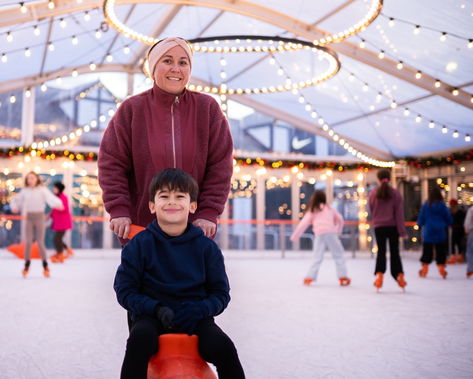 A child being pushed on an orange skate aid by a smiling adult